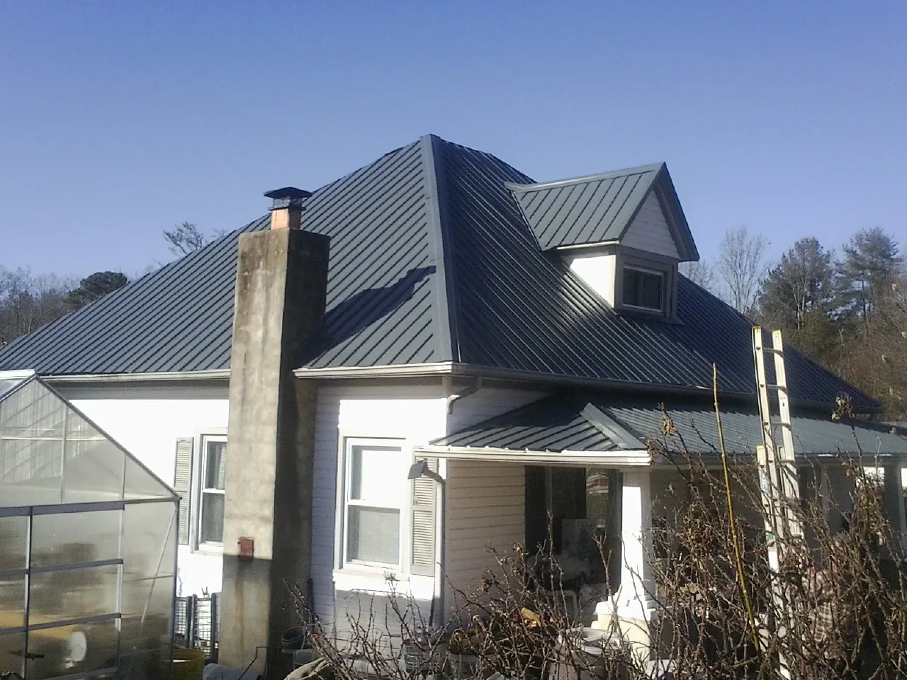 Dark blue standing seam metal roof on a white farmhouse with dormer — Slate & Tile Roof Repair by Roofing Brothers in Centerport
