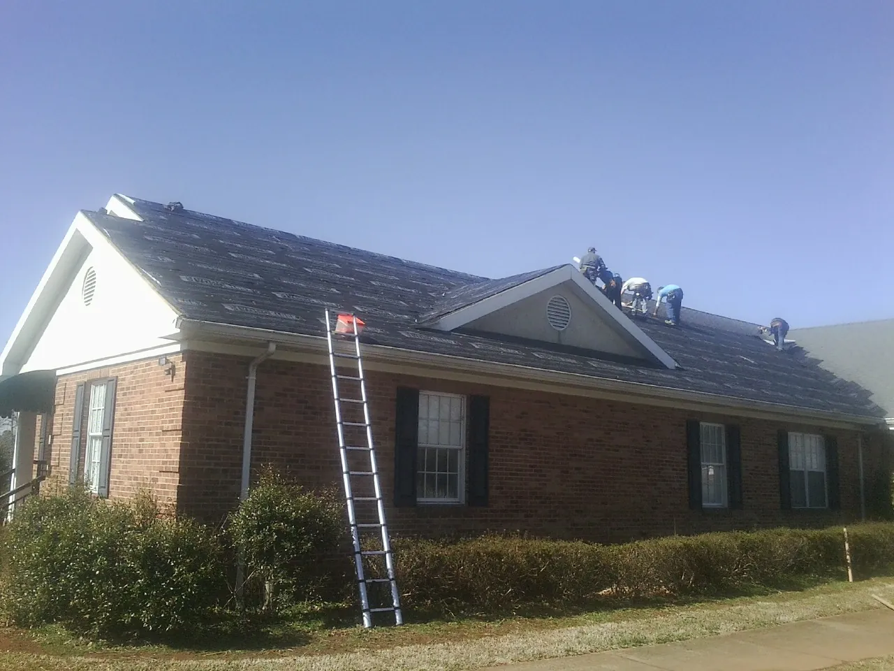 Crew tearing shingles off a brick ranch roof with a ladder set — Metal Roof Repair work by our crew in Centerport