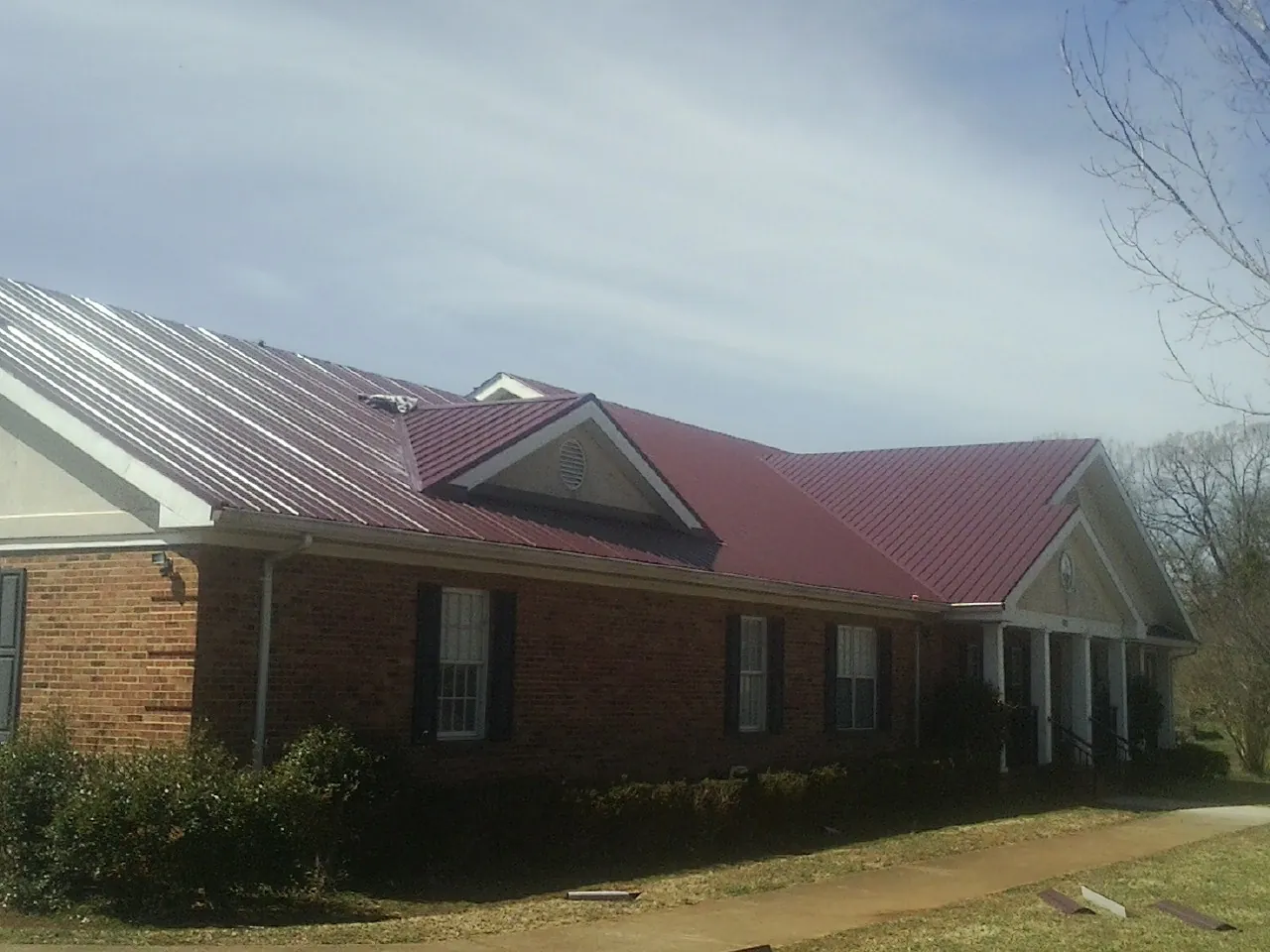 Red metal roof with gabled entries on a long brick building, from a Hail Damage Roof Repair job in Centerport