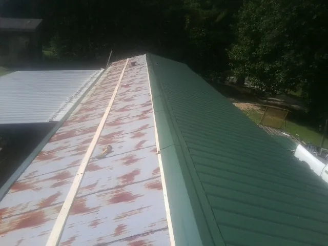 Old rusted panels beside newly installed green metal roofing — Wind Damage Roof Repair by Roofing Brothers in Centerport