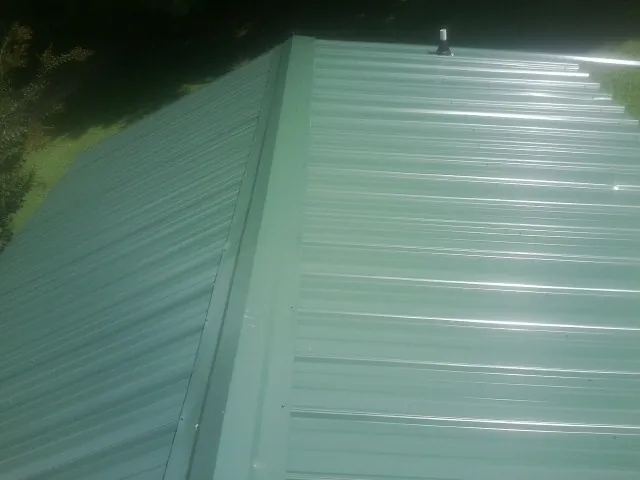New green metal panels meeting at the ridge of a roof — Flat Roof Repair work by our crew in Centerport