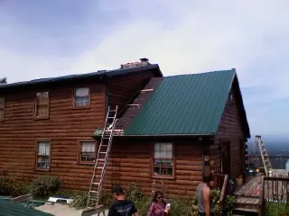 Green metal roof going on a two story log home with ladders set in Centerport