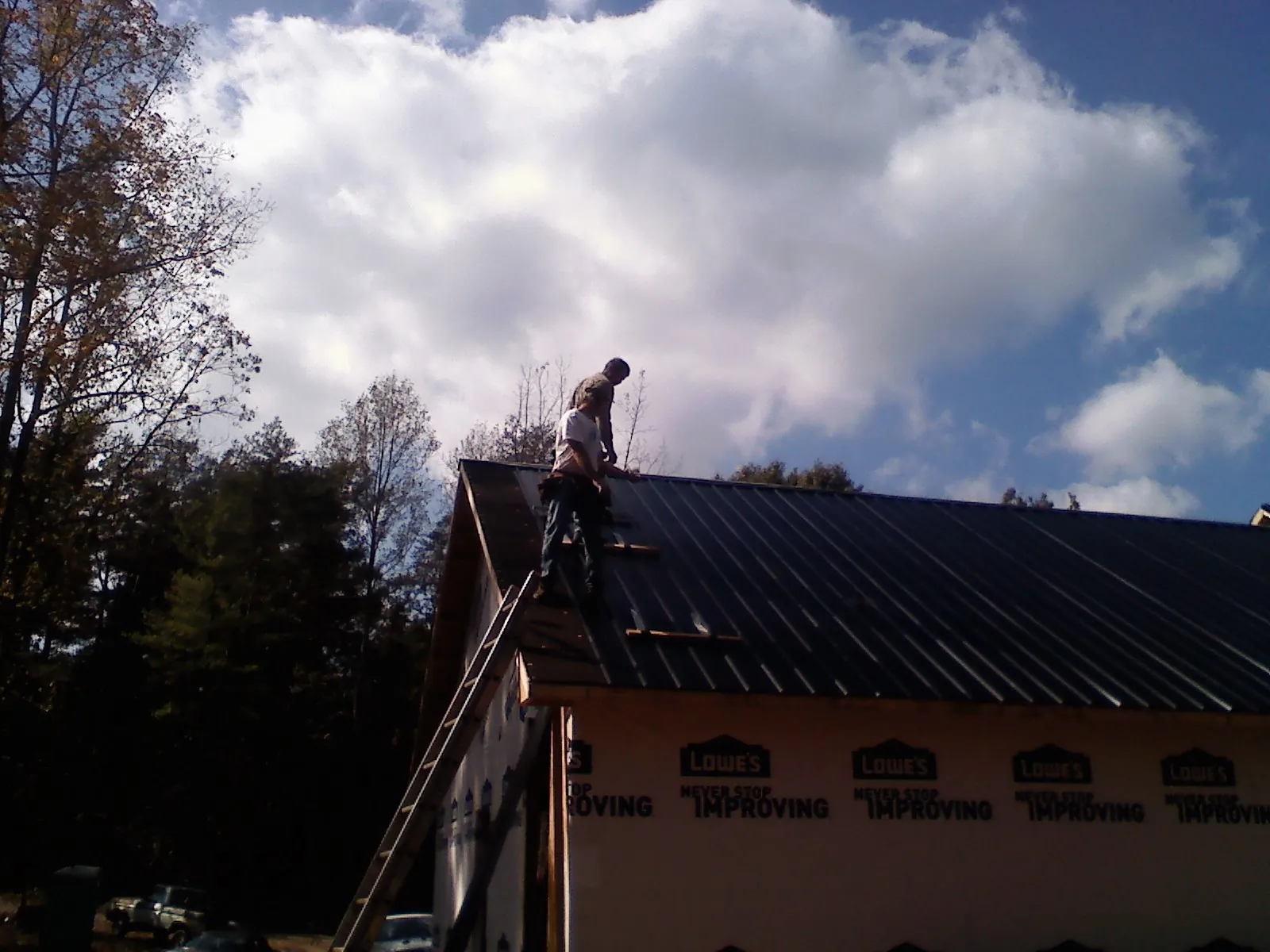 Roofer fastening dark metal panels high against a cloudy sky, from a Roof Inspection job in Centerport