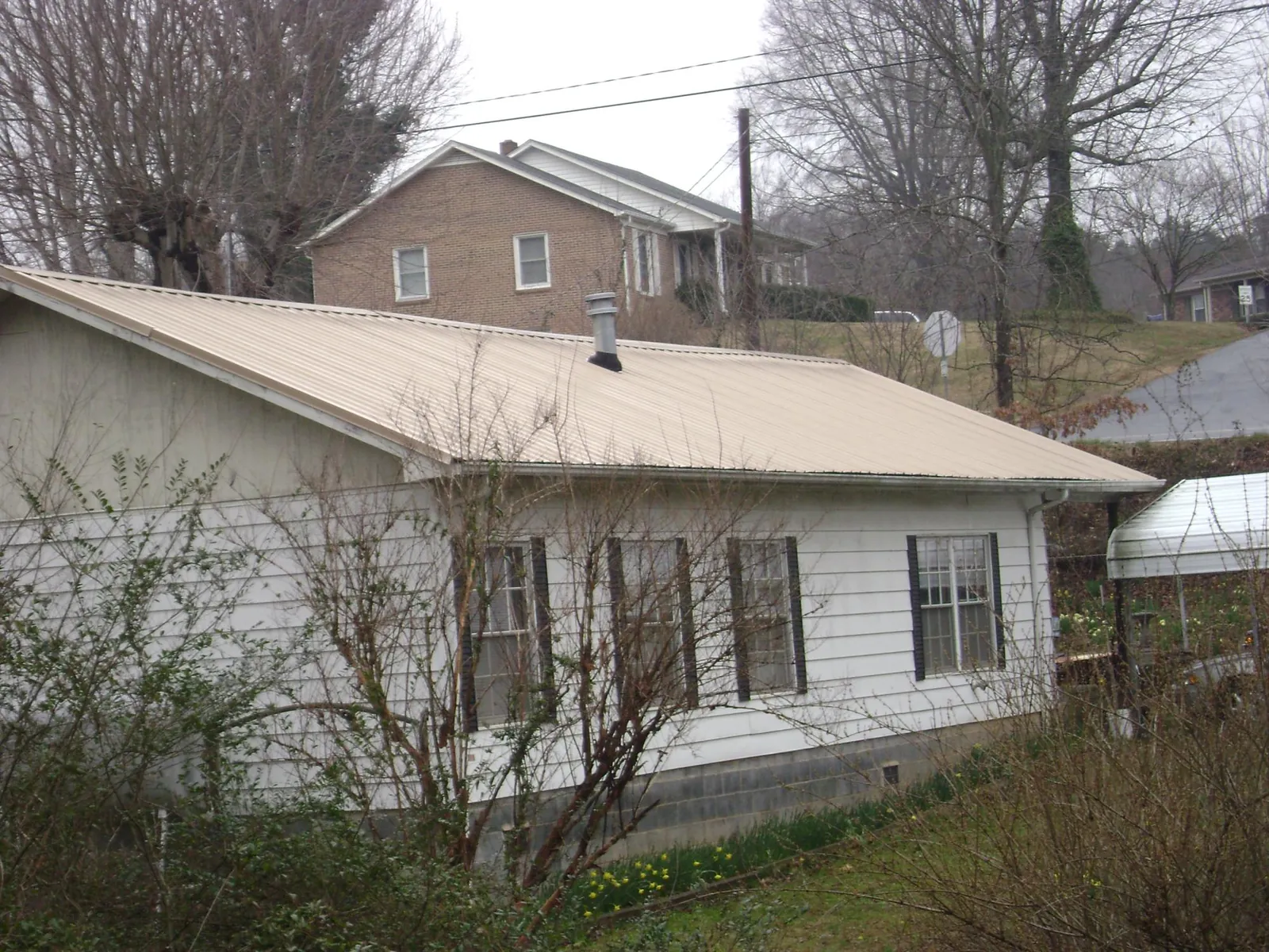 Tan metal roof on a white sided house set into a hillside — Commercial Roofing by Roofing Brothers in Centerport